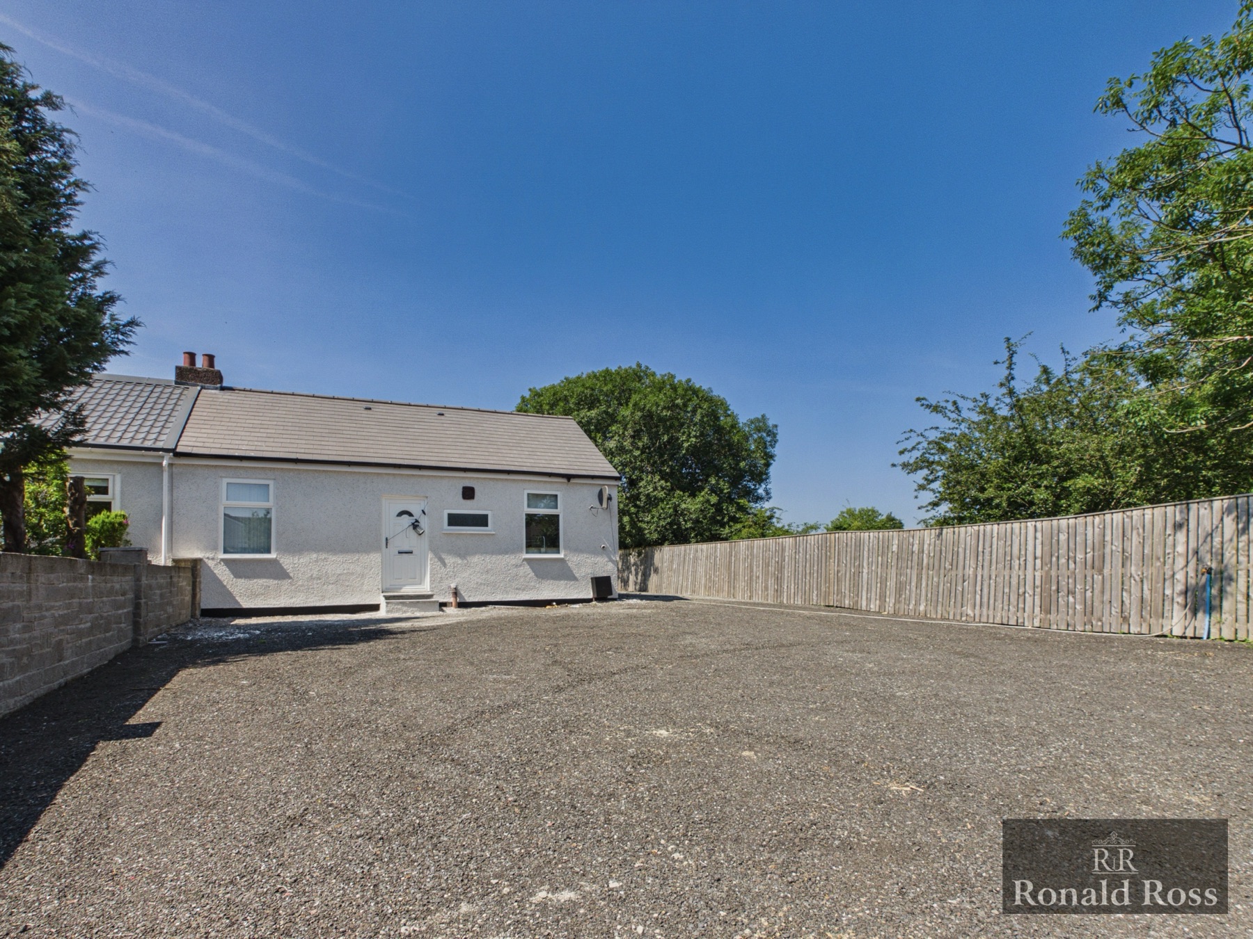 A white rendered cottage with a large gravel driveway from a Ronald Ross listing